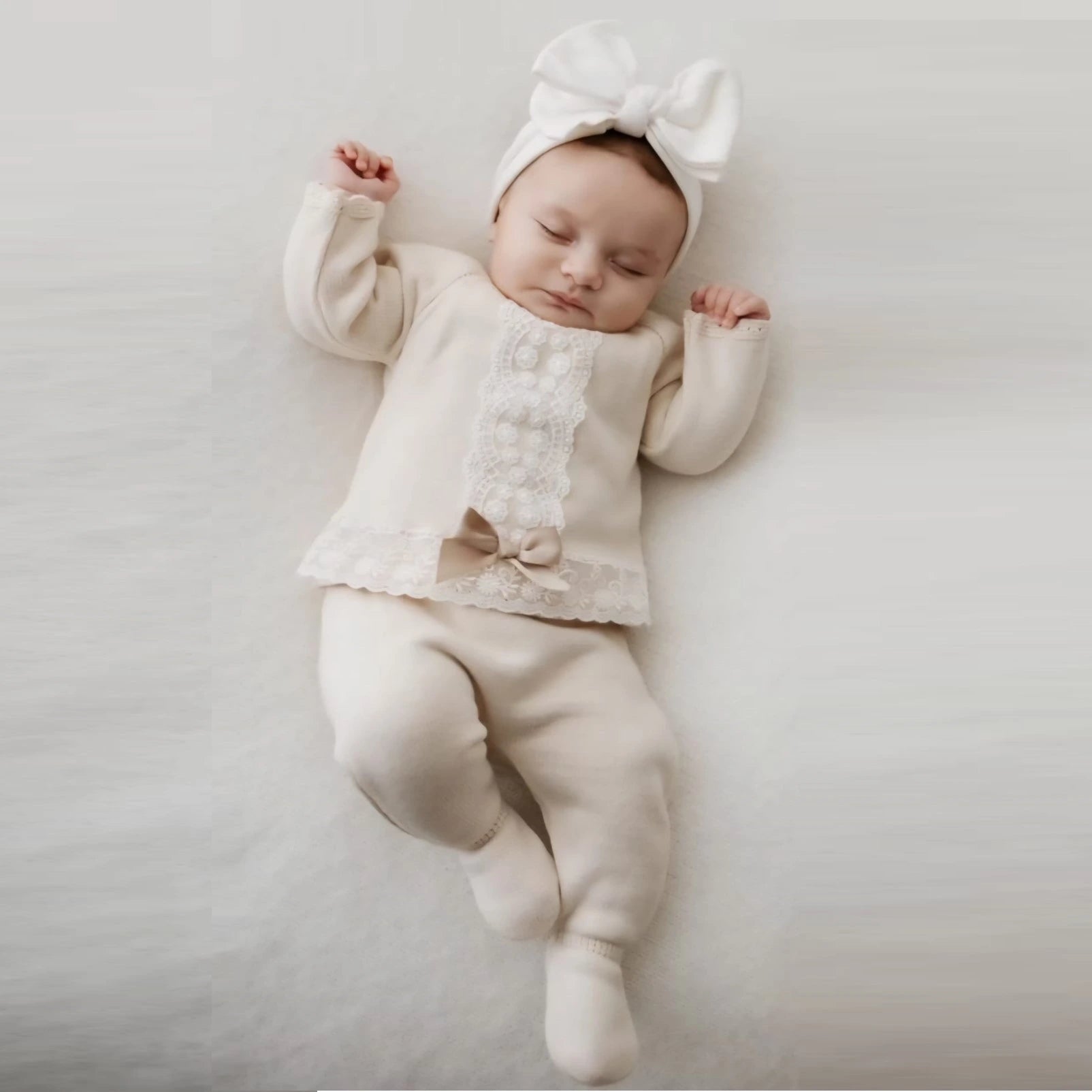 Baby in a white outfit with a bow on a light gray background