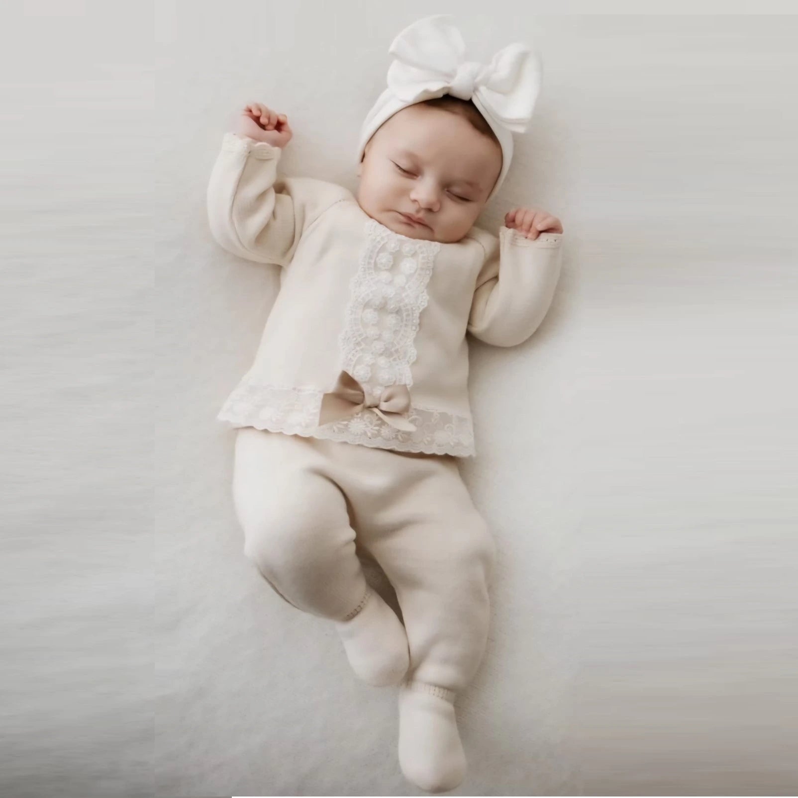 Baby in a white outfit with a bow on a light gray background