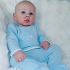 Baby wearing a light blue knitted outfit on a white fluffy blanket