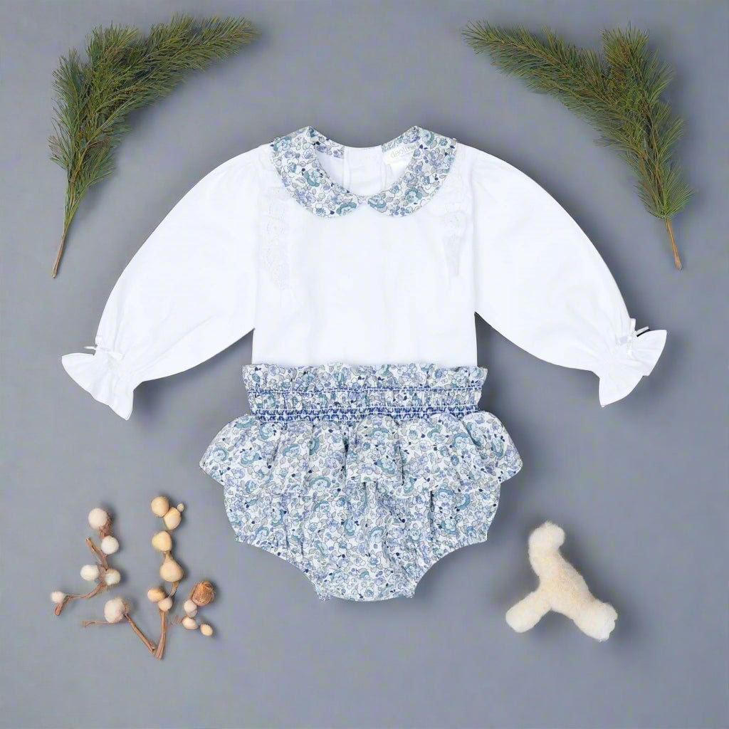 Baby outfit with white long-sleeve top and floral bloomers on a black background