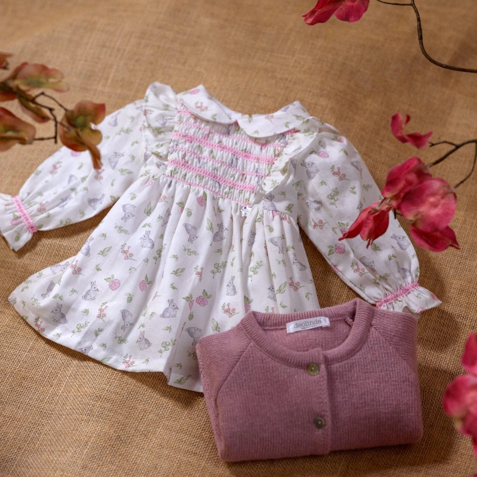 Floral dress and pink sweater on a textured surface with flowers.