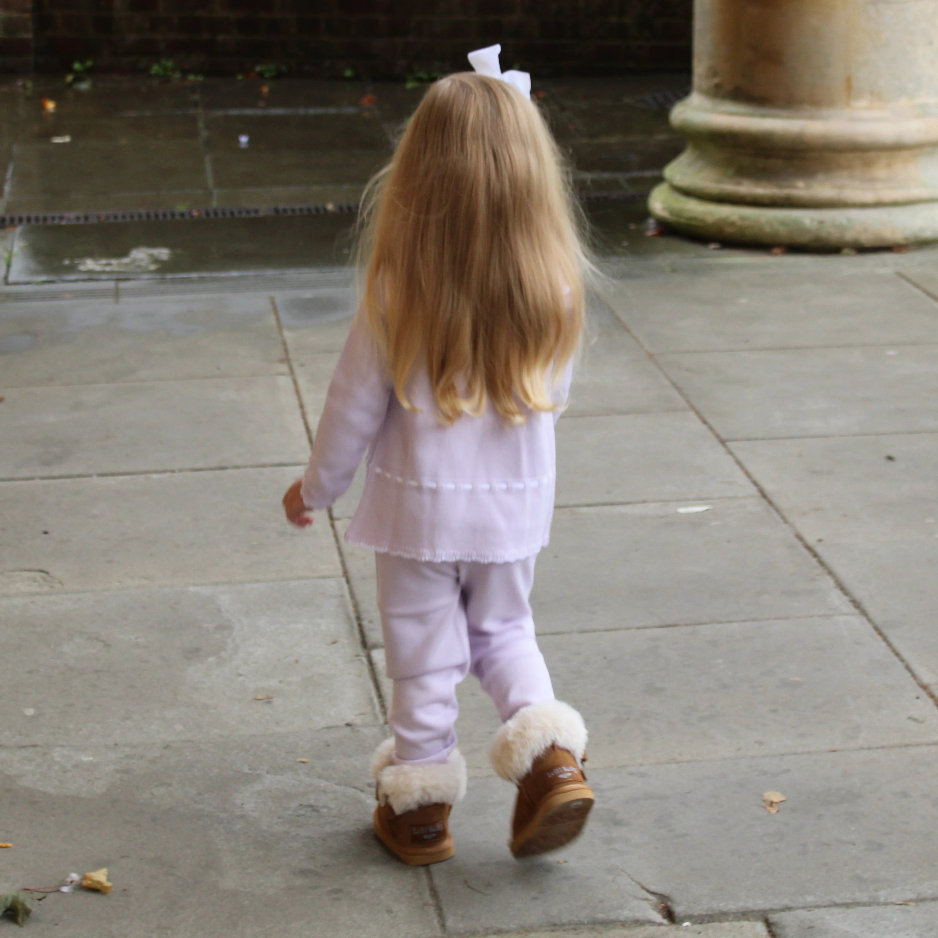Child in a light purple outfit with fur-lined shoes walking on a stone path.