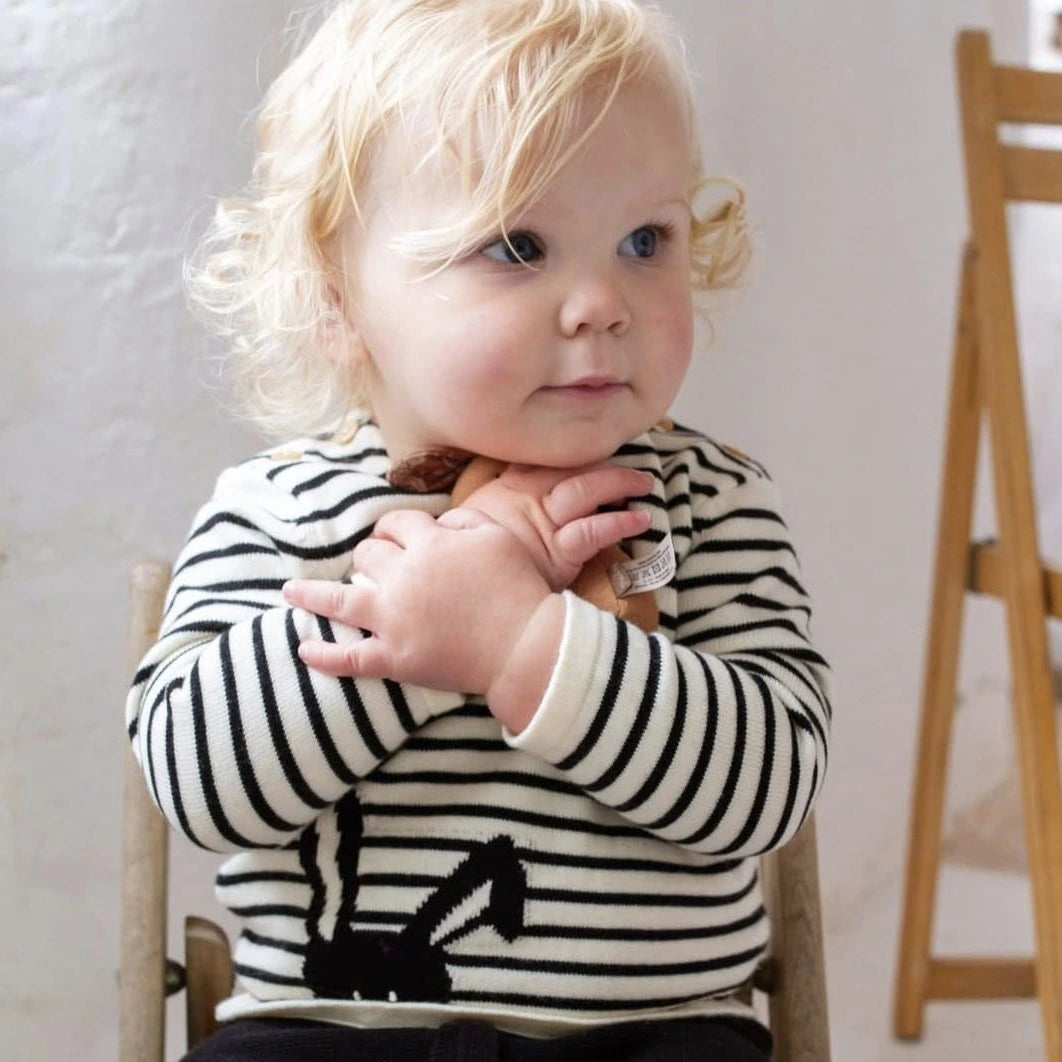 Child wearing a black and white striped sweater with a small animal design, sitting on a chair.