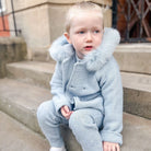 Child wearing a light blue outfit with fur trim sitting on steps.
