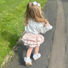 Child in a white blouse and pink skirt walking on a path with grass on one side.