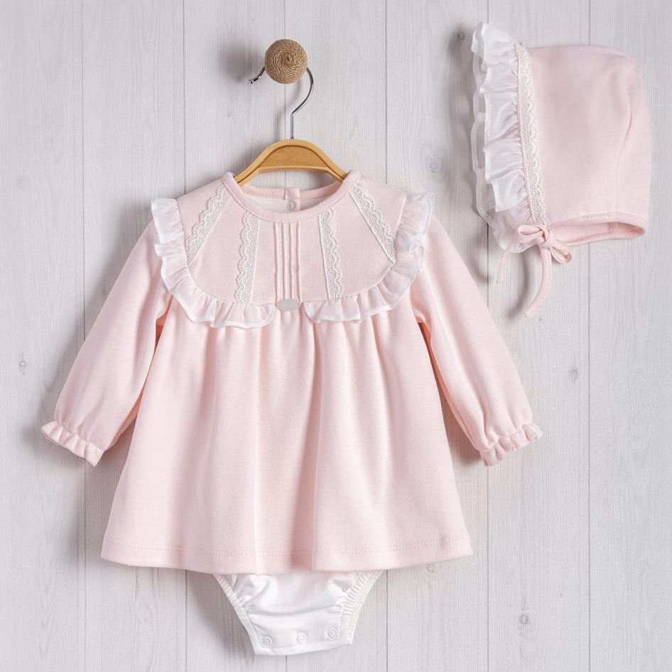 Pink baby outfit with top and pants hanging on a wooden hanger against a light wooden background.