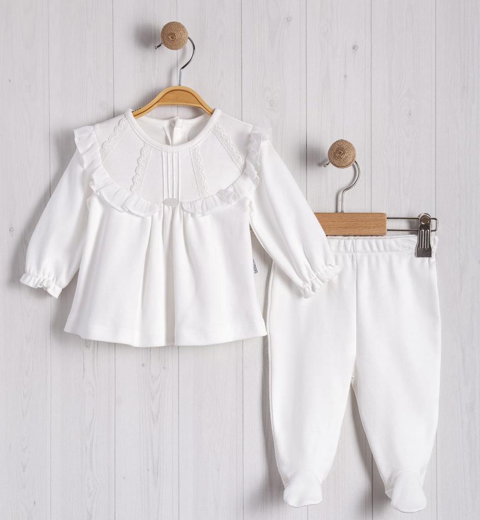 White children's outfit with a top and pants on wooden hangers against a light wooden panel background.