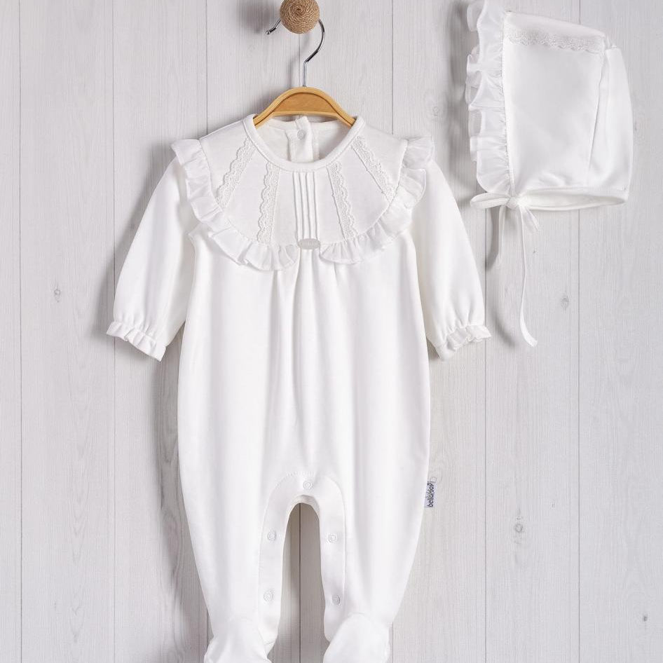 White baby romper with ruffled collar and matching bonnet on a wooden hanger against a light wooden panel background.