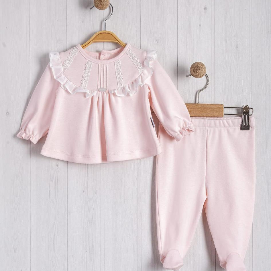 Pink baby outfit with top and pants hanging on a wooden hanger against a light wooden background.