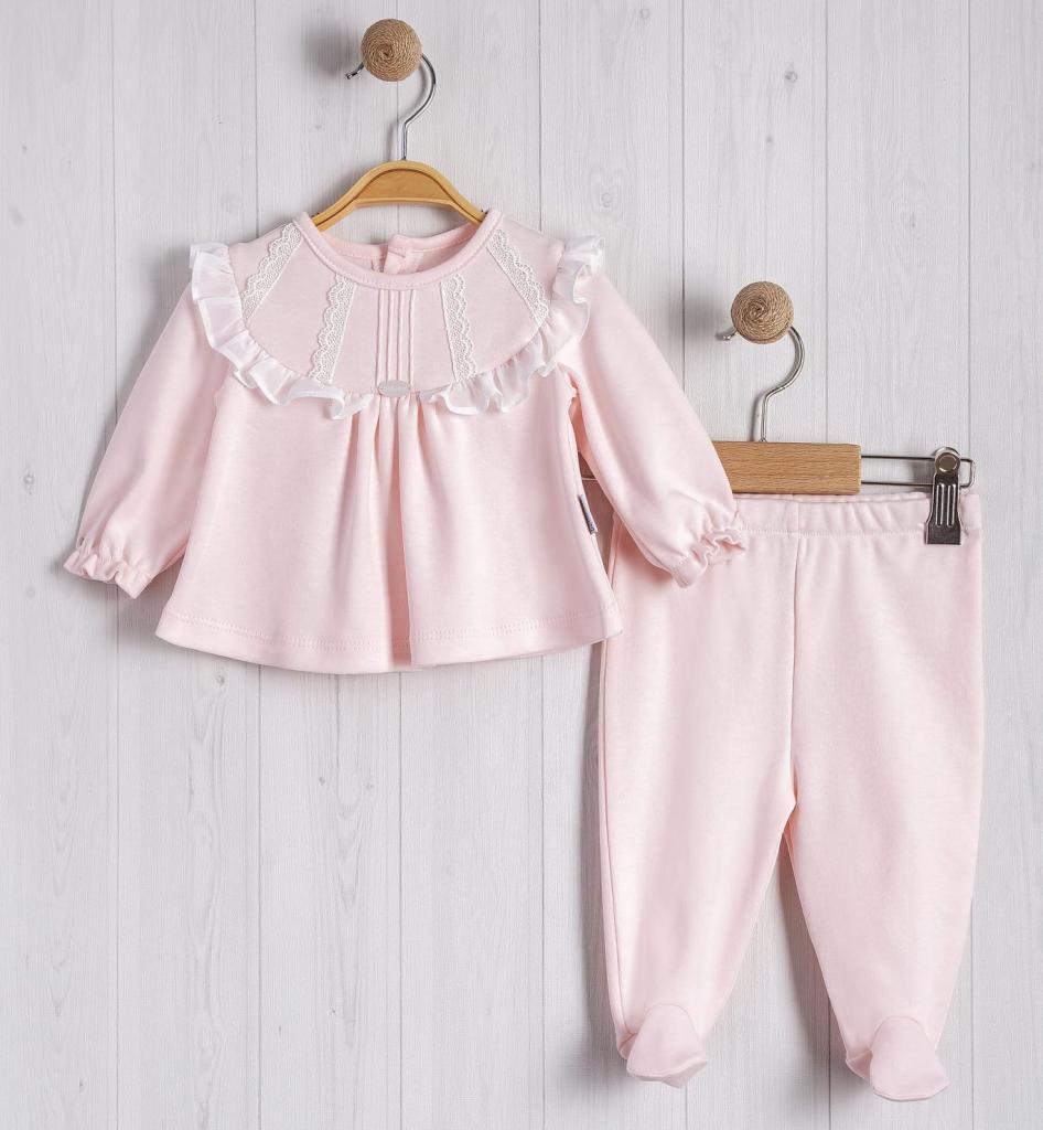 Pink baby outfit with top and pants hanging on a wooden hanger against a light wooden background.