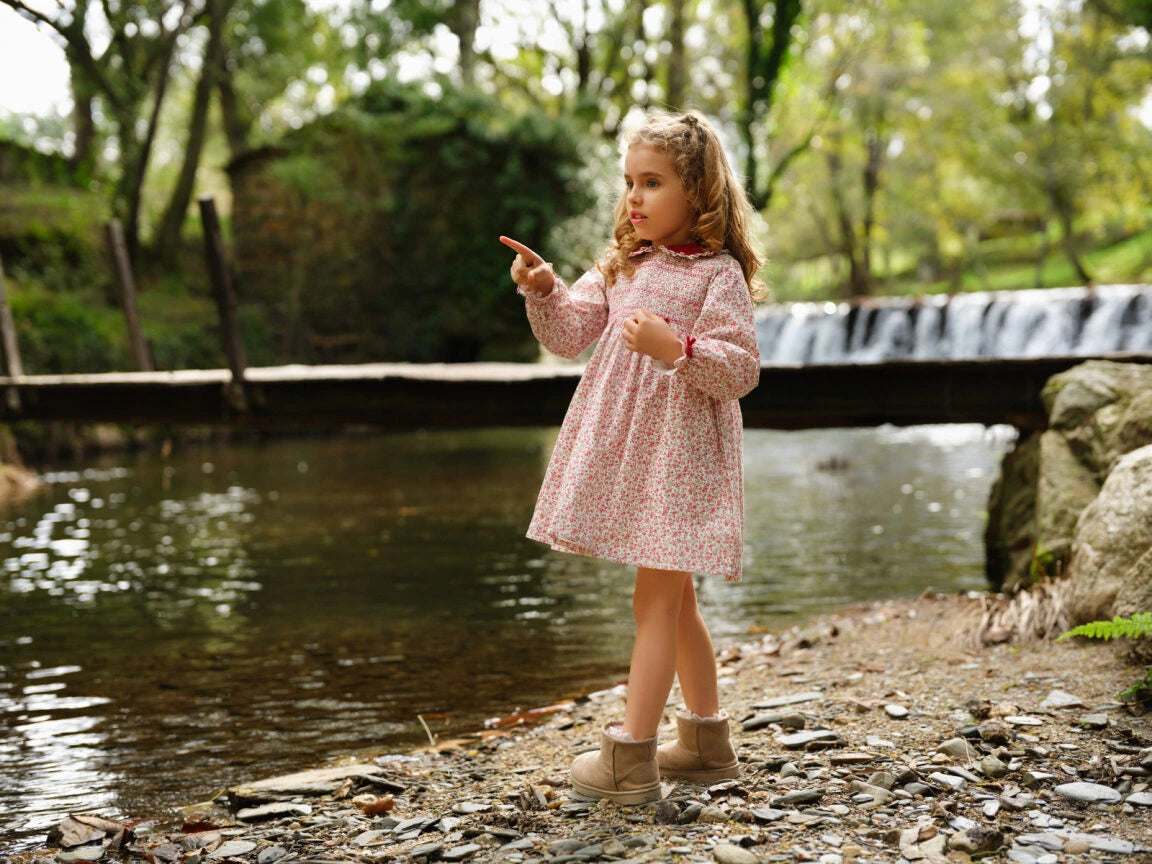 Young girl in a pink dress standing by a stream with a bridge in the background