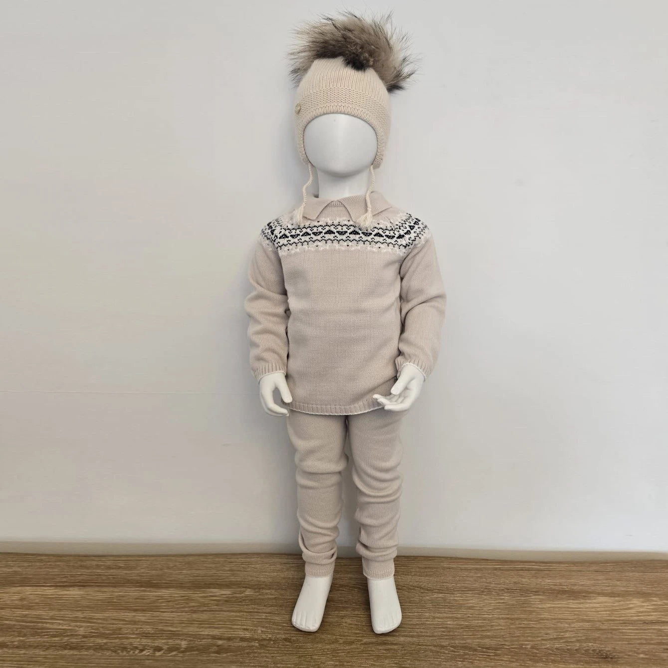 Mannequin wearing a beige outfit with a patterned collar and matching hat on a wooden floor.