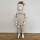 Mannequin wearing a beige outfit with a patterned collar and matching hat on a wooden floor.