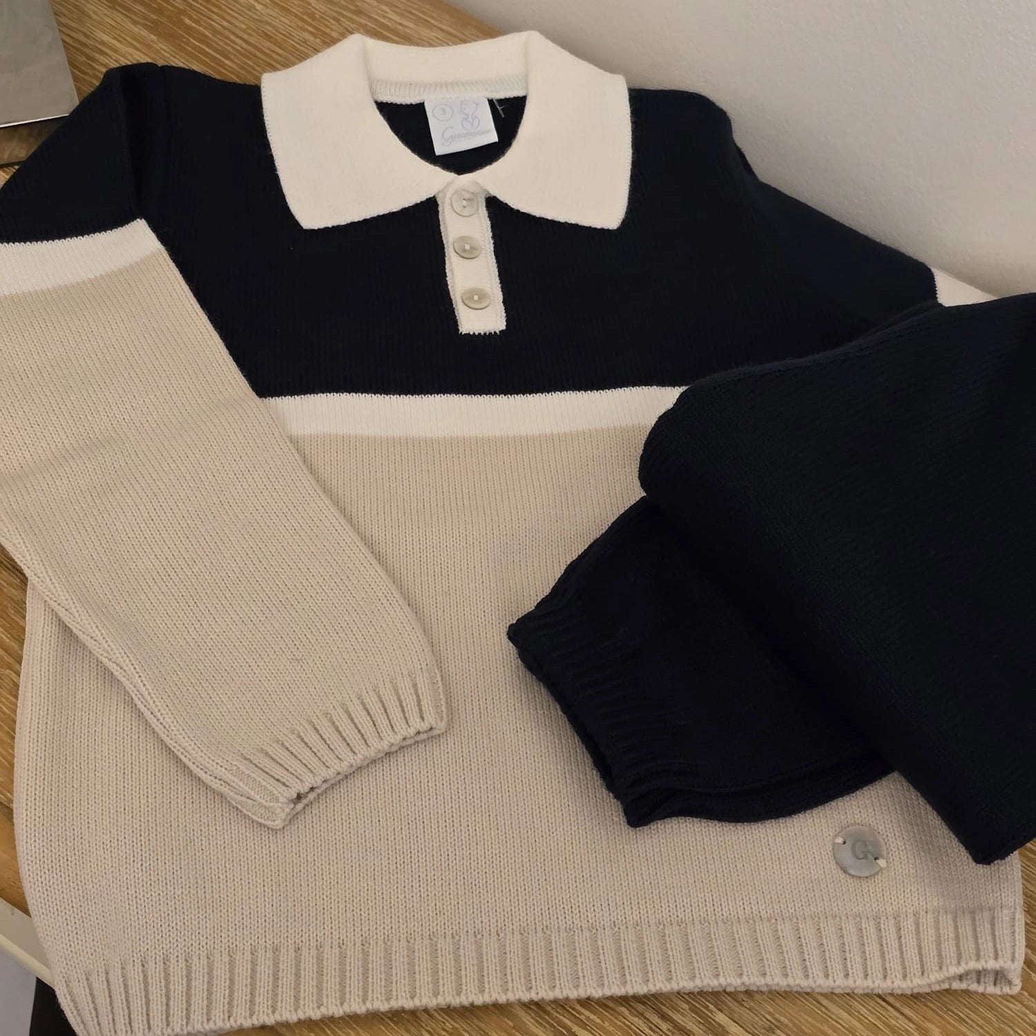 Black and beige striped sweater with buttons on a wooden surface