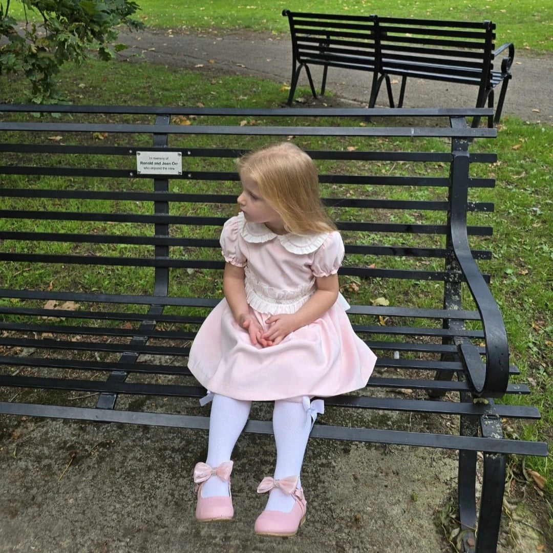 Young girl in a pink dress sitting on a black metal bench in a park.
