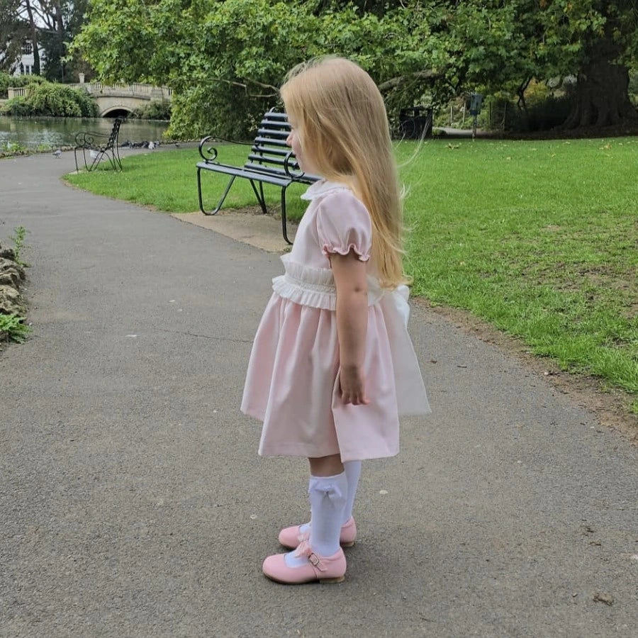 Young girl in a pink dress standing on a path in a park.