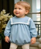 Child wearing a light blue dress with white trim standing outdoors.