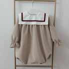 Beige baby dress with white collar and red trim on a hanger against a white background