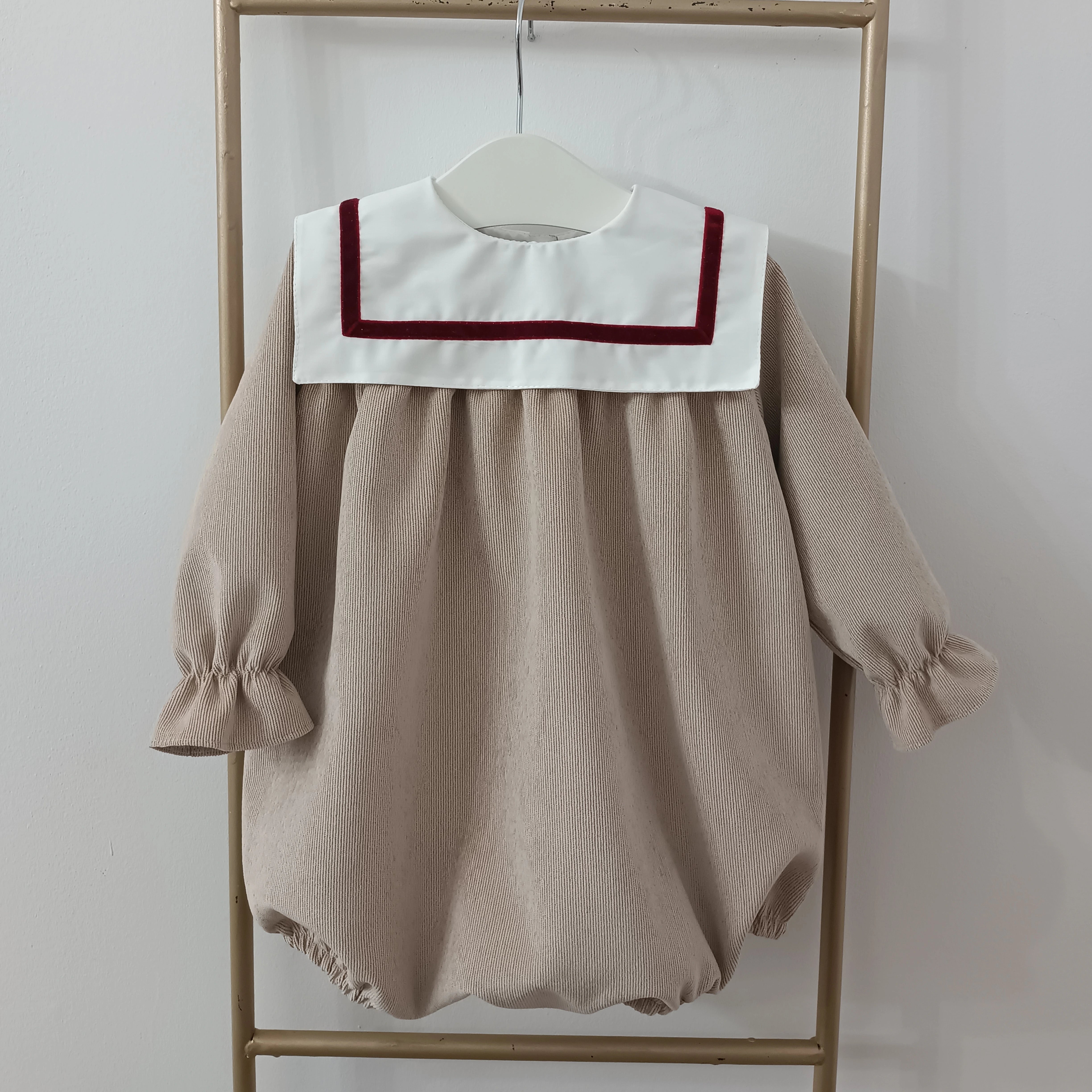 Beige baby dress with white collar and red trim on a hanger against a white background
