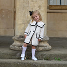 Young girl in a white coat with black trim standing on stone steps.