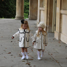 Two young girls in matching white coats walking outdoors on a stone path.