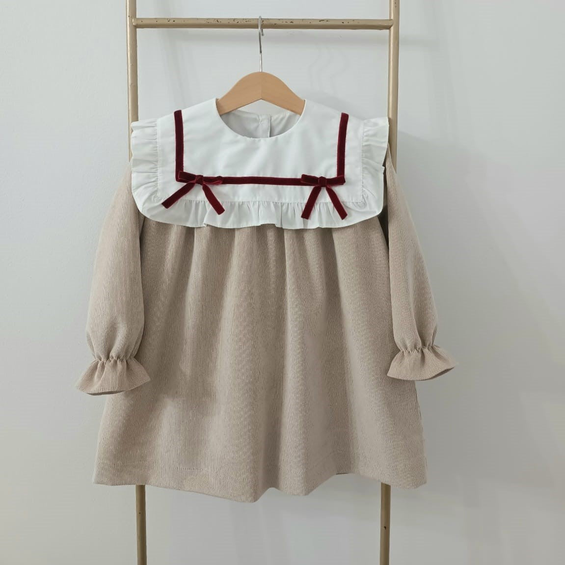 Beige dress with white collar and red details on a wooden hanger against a white background