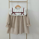 Beige dress with white collar and red details on a wooden hanger against a white background