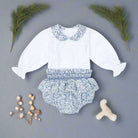 Baby outfit with white long-sleeve top and floral bloomers on a black background