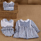 Baby outfit set with floral dress, bloomers, and headband on a brown fabric background