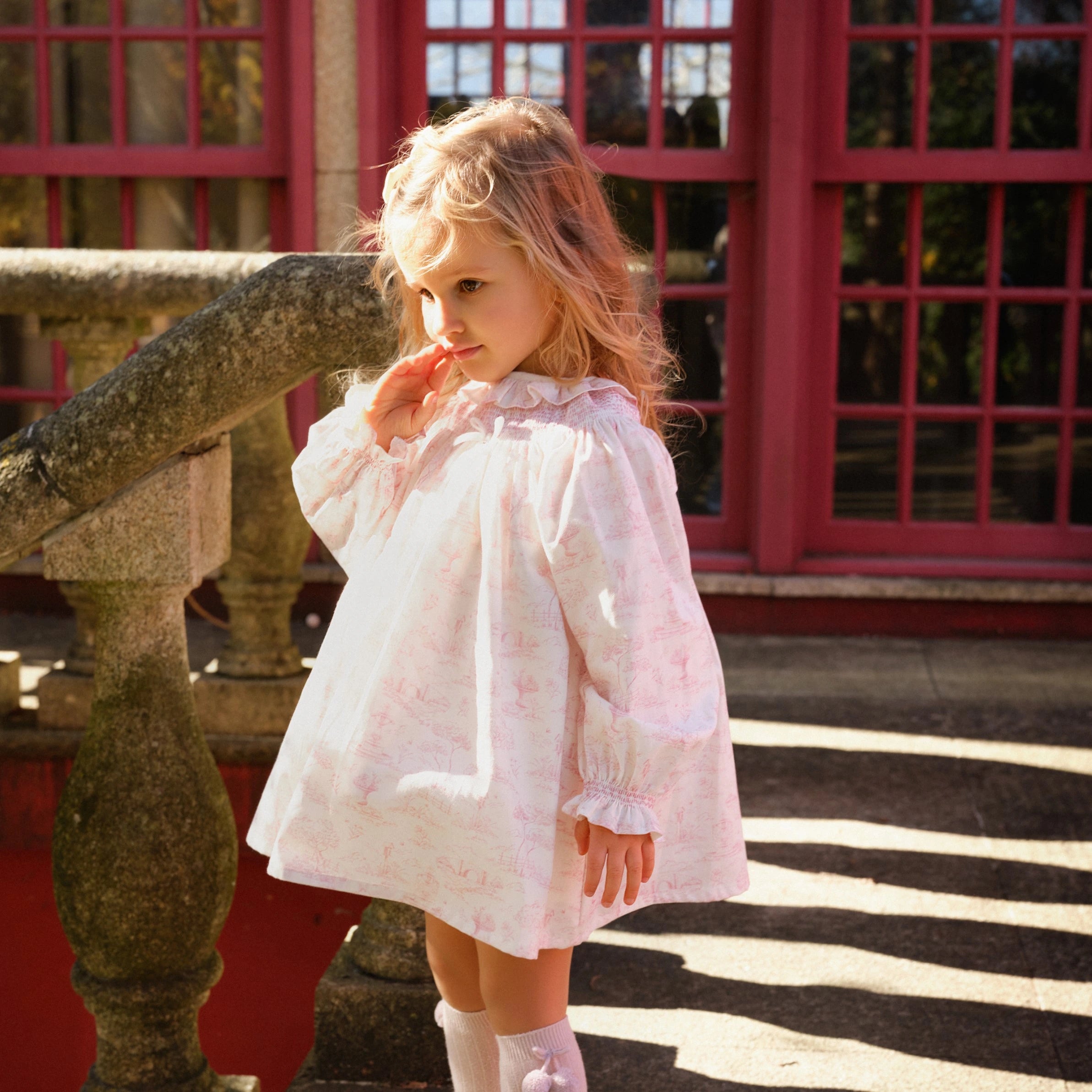 Young girl in a white dress standing in front of a red building.