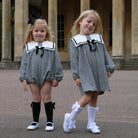 Two young girls in matching black and white checkered outfits with sailor collars standing outdoors.