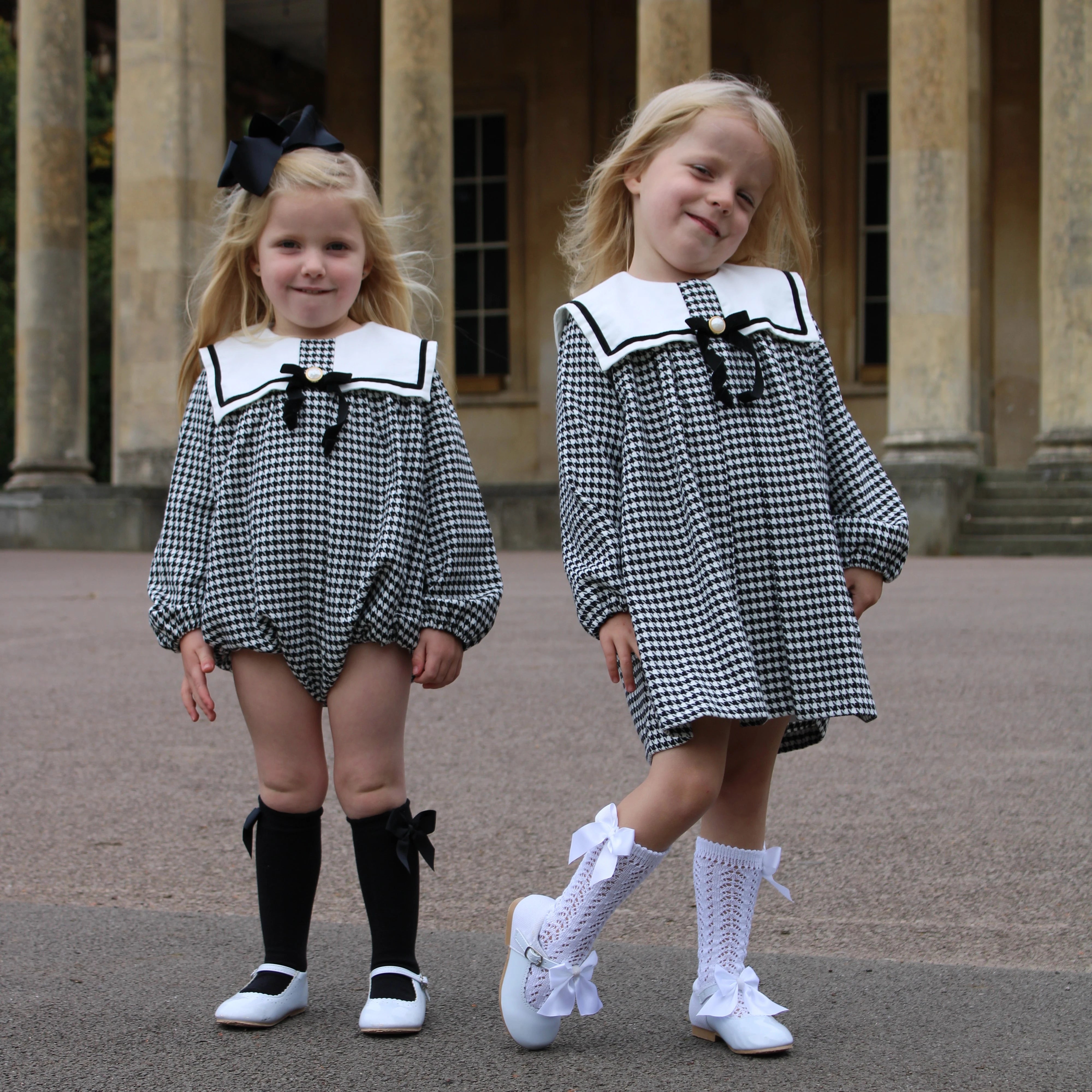 Two young girls in matching black and white checkered outfits with sailor collars standing outdoors.