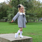 Young girl in a black and white checkered dress with a bow standing on a stone block in a park.