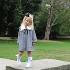 Young girl in a black and white checkered dress with a bow standing on a stone path in a park.
