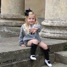 Young girl in a checkered dress with a black bow sitting on stone steps.