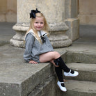 Young girl in a checkered outfit with a large bow sitting on stone steps.