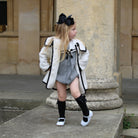 Young girl in a white coat with black trim, black knee-high socks, and white shoes standing on stone steps.
