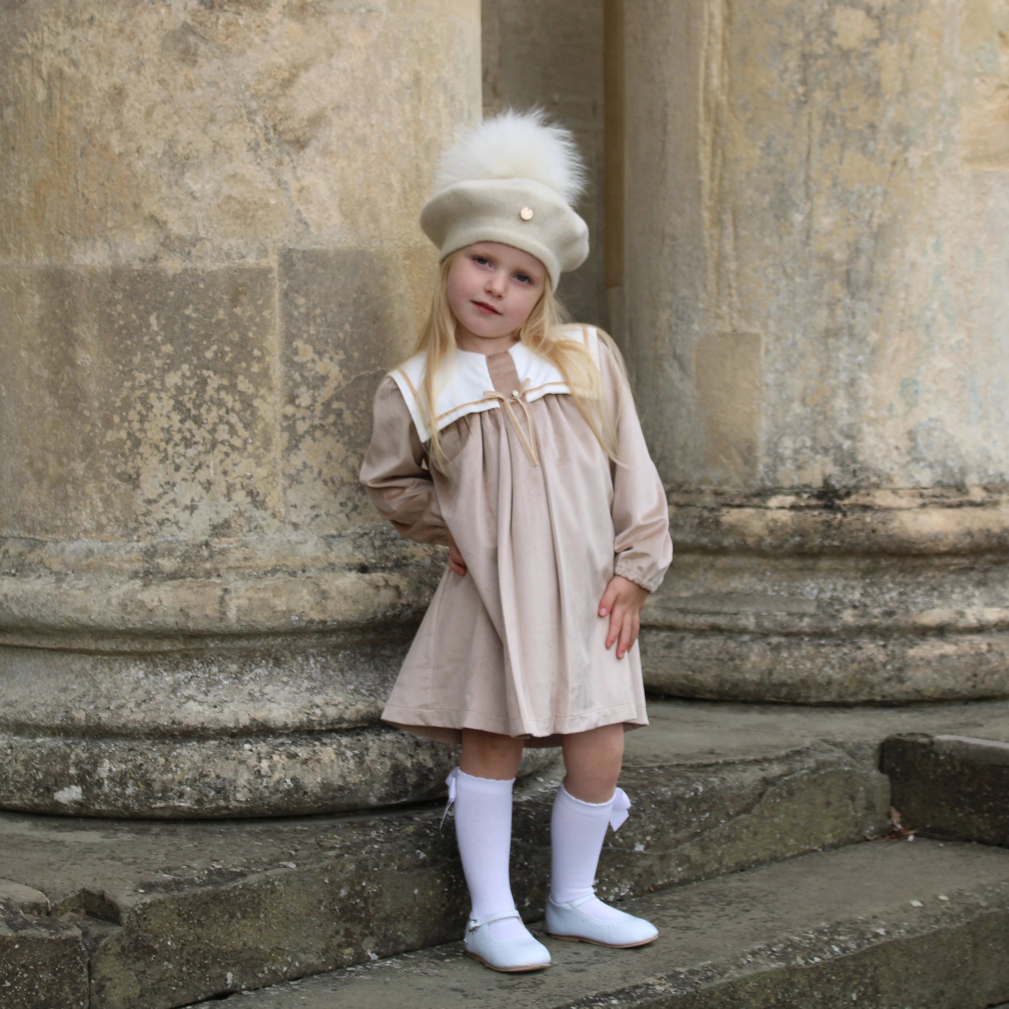 Young girl in a beige dress and white hat standing on stone steps.