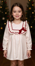 Young girl wearing a Pink dress with Burgundy accents in front of a decorated Christmas tree.