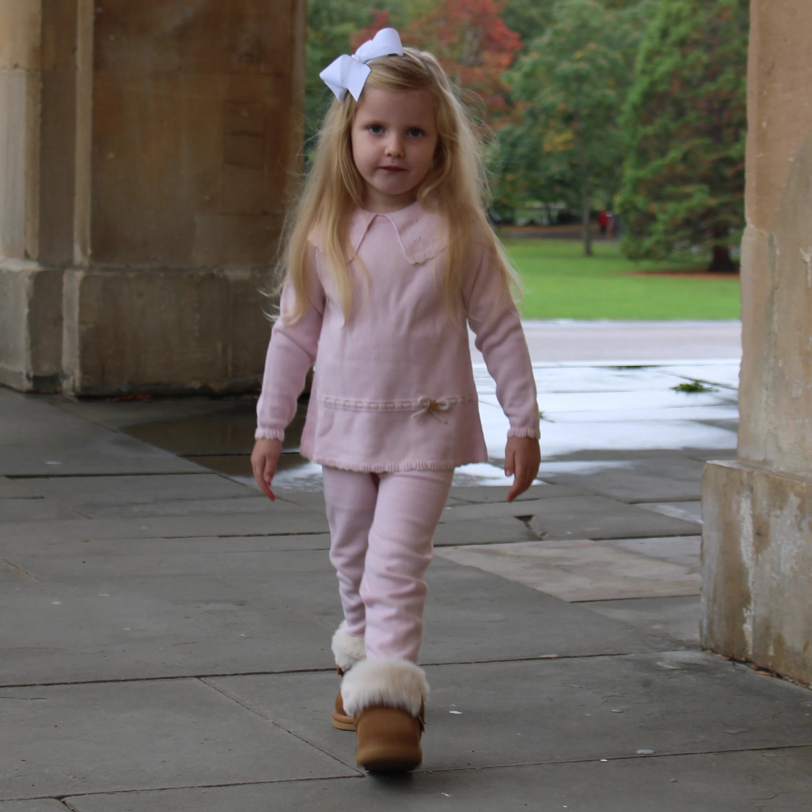 Young girl in a pink outfit walking outdoors on a stone path.