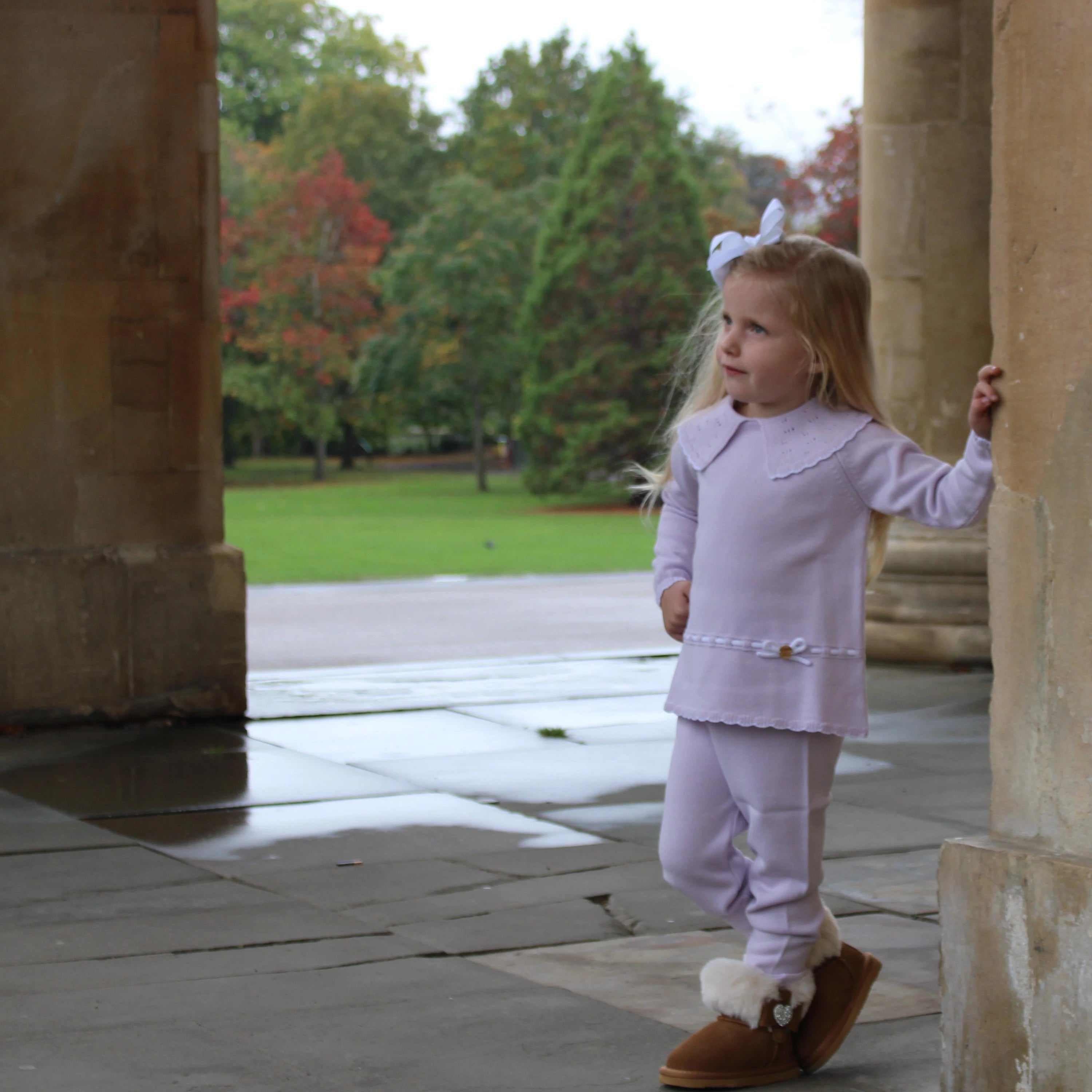 Young girl in a light purple outfit with bunny ears standing between stone columns.