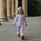 Young girl in a light purple outfit with white collar and brown boots walking on a stone path.
