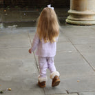 Child in a light purple outfit with fur-lined shoes walking on a stone path.