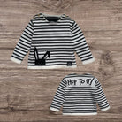 Black and white striped children's sweatshirt with a bunny design on a wooden surface