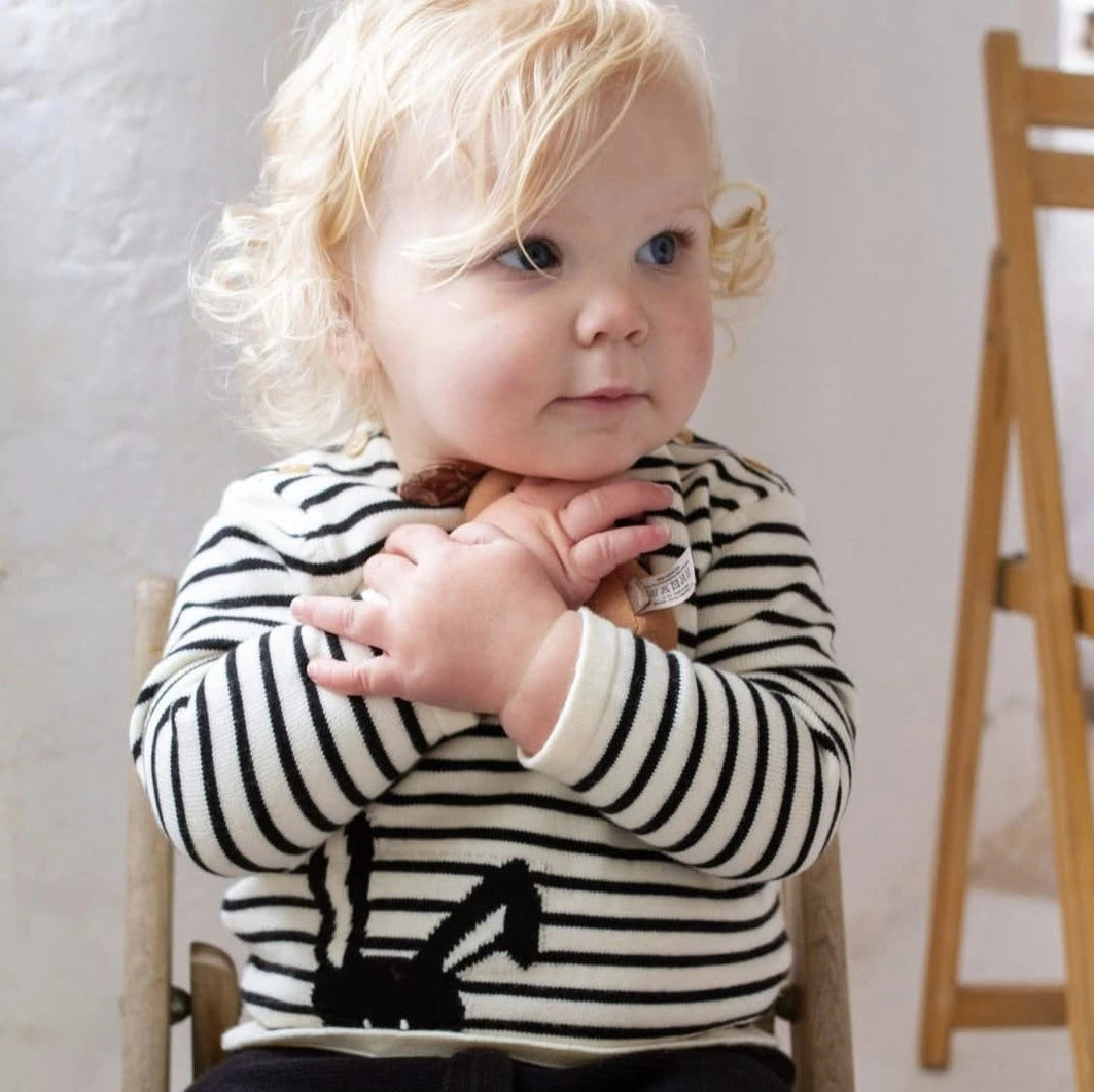 Child wearing a black and white striped sweater with a small animal design, sitting on a chair.
