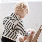 Child wearing a striped sweater with 'Hop to it!' text, holding a teddy bear.