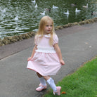Young girl in a pink dress standing on a path near a pond with ducks.