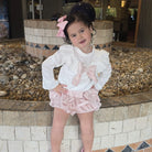 Young girl in a white blouse and pink skirt standing in front of a decorative fountain.