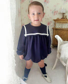Child wearing a navy dress with white trim in a room with floral wallpaper.