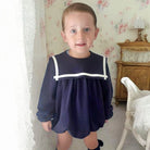 Child wearing a navy dress with white trim in a room with floral wallpaper.